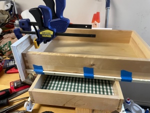 Empty wooden drawer with side sliders taped on with blue tape and a facing clamped on with a couple of clamps.